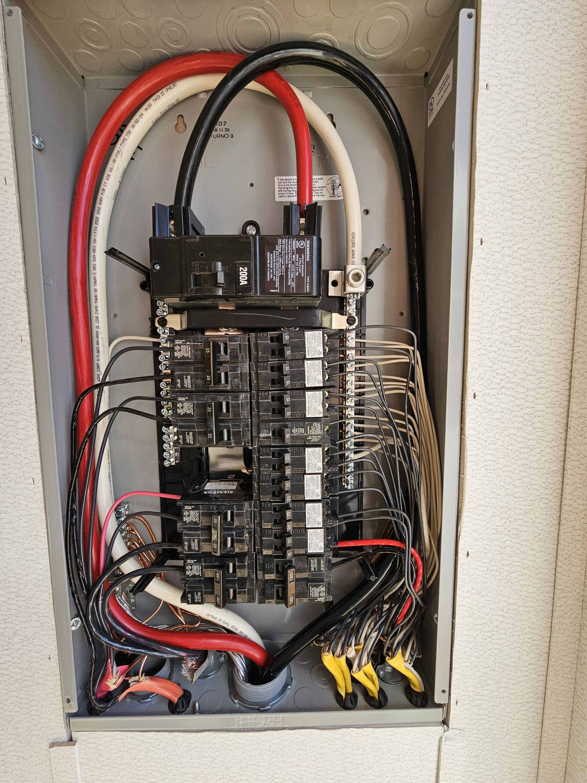 An open electrical breaker panel showing multiple circuit breakers, neatly organized wires, and connected cables of various colors.